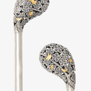 May include: Two silver walking sticks with ornate handles. The handles are made of silver and are decorated with a floral design. The flowers are made of silver and are accented with gold. The sticks are a traditional Japanese design.