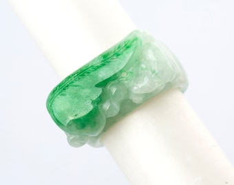 Könnte beinhalten: Ein grüner Jade-Ring mit einem geschnitzten Design aus einem Blatt und einer Blume. Der Ring ist aus durchscheinendem Jade gefertigt und hat eine glatte, polierte Oberfläche.