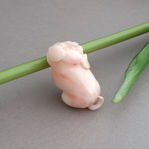 Peut inclure: Une sculpture en corail rose d'une petite figurine dodue avec une t&ecirc;te ronde et une petite queue. La sculpture est lisse et polie, avec une d&eacute;licate teinte rose.