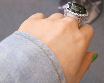 Könnte beinhalten: Ein silberner Ring mit einem großen grünen Edelstein, der in einem floralen Design gefasst ist.