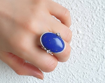May include: A silver ring with a large oval blue stone and smaller clear stones on the side.