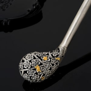 May include: A silver and gold decorative handle with a floral design. The handle is intricately carved with flowers and birds.