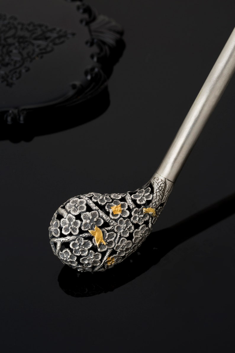 May include: A silver and gold decorative handle with a floral design. The handle is intricately carved with flowers and birds.