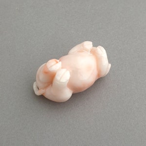 Peut inclure: Une petite figurine de cochon en corail rose. Le cochon est couch&eacute; sur le dos, les pattes en l'air.