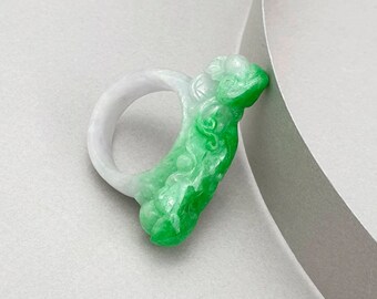 Könnte beinhalten: Ein grüner und weißer Jaderinge mit einem geschnitzten Design. Der Ring ist aus glattem, poliertem Jade gefertigt und hat ein zartes, filigranes Design.