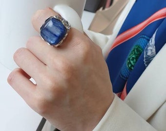May include: A silver ring with a blue gemstone. The ring is on a person's finger. The person is holding a white coffee mug.