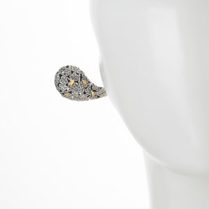 May include: A silver and gold floral-shaped earring with a textured surface.