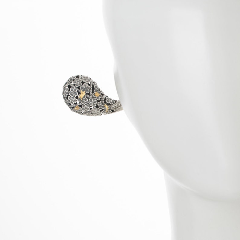 May include: A silver and gold floral-shaped earring with a textured surface.