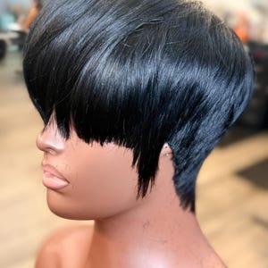 May include: A mannequin head featuring a short, sleek, jet-black hairstyle with a blunt-cut fringe that covers the forehead and straight, textured layers that taper toward the nape of the neck, showcasing a smooth, glossy finish throughout.