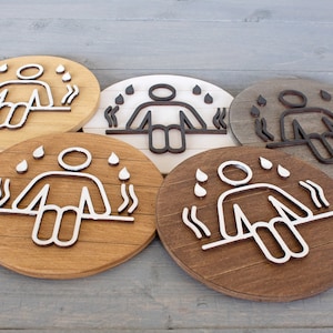 May include: Four wooden signs with different coloured backgrounds and a white or black outline of a person sitting with steam rising around them. The signs are all round and have a wood grain texture.