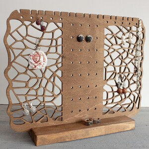 May include: Wooden earring stand with a decorative laser cut design. The stand has multiple holes for hanging earrings and a base for storing rings or other jewelry.