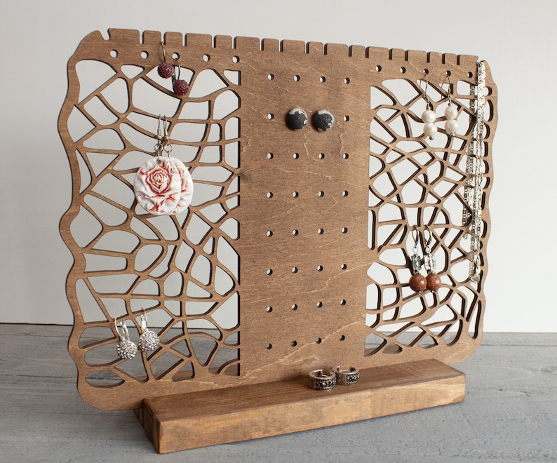 May include: Wooden earring stand with a decorative laser cut design. The stand has multiple holes for hanging earrings and a base for storing rings or other jewelry.