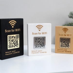 Op de afbeelding: Drie rechthoekige houten bordjes in zwarte, witte en natuurlijke houtafwerking. Elk bordje heeft een lasergegraveerd wifi-symbool, de tekst Scan for WIFI, een metalen QR-codeplaatje en de tekst Network: guest Password: 123456789.