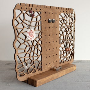 May include: Wooden earring stand with a geometric design and multiple holes for hanging earrings. The stand has a base for storing rings or other jewelry.
