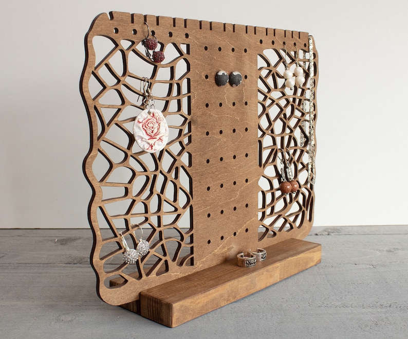May include: Wooden earring stand with a geometric design and multiple holes for hanging earrings. The stand has a base for storing rings or other jewelry.