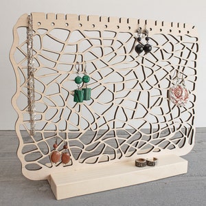 May include: Wooden jewellery stand with a delicate, intricate design. The stand features a large, open area for hanging earrings and a smaller base for rings or bracelets. The stand is made of light-coloured wood and has a natural finish.