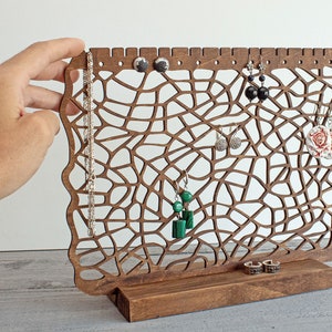 May include: Wooden jewellery stand with a delicate, intricate design. The stand features a variety of hooks and slots for holding earrings, necklaces and bracelets. The stand is made of dark brown wood and has a natural finish.