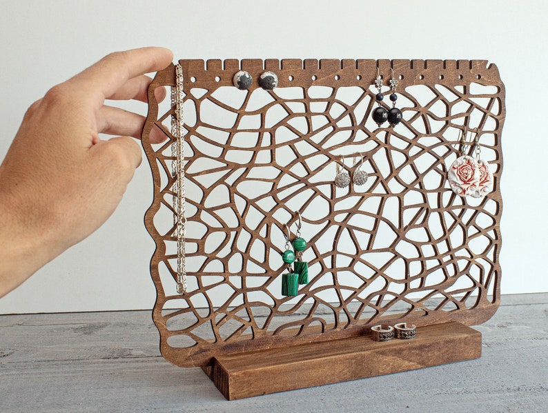 May include: Wooden jewellery stand with a delicate, intricate design. The stand features a variety of hooks and slots for holding earrings, necklaces and bracelets. The stand is made of dark brown wood and has a natural finish.