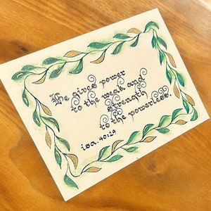 Elegante postal hecha a mano con Isaías 40:29: caligrafía atemporal en cartulina color crema, detalles dorados y opción de montaje en verde damasco