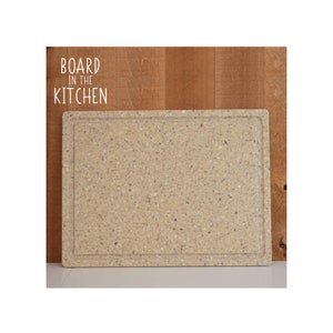 May include: A beige rectangular cutting board with a speckled surface. The board has a slightly raised edge around the perimeter.