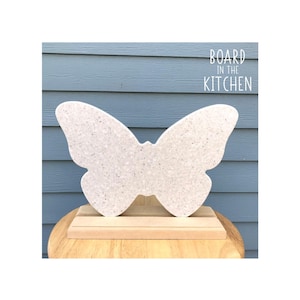 May include: White butterfly-shaped cutting board with a speckled finish, standing on a wooden base. The text "BOARD IN THE KITCHEN" is printed above the board.