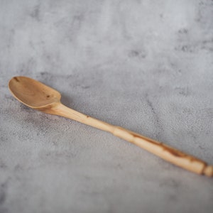 May include: A wooden spoon with a natural finish. The spoon has a long handle and a rounded bowl.