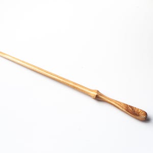 Op de afbeelding: Een lange, slanke houten roerstaaf met een lichtbruine afwerking en een natuurlijk houtnerfpatroon. De staaf heeft een taps toelopend, puntig uiteinde en een iets breder, afgerond handvat voor een comfortabele grip tijdens het roeren.
