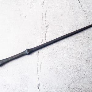 May include: A dark brown wooden wand with a rounded tip. The wand is lying on a white textured surface.