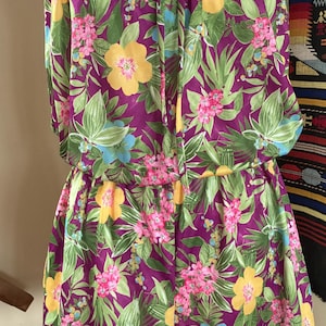 May include: A strapless romper with a vibrant floral print. The fabric features a deep purple background with yellow, pink, and blue flowers, and green leaves. The romper has a drawstring at the top and waist, creating a flattering silhouette.