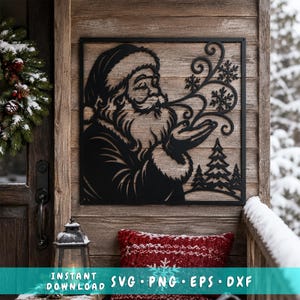May include: A black metal wall art piece featuring a silhouette of Santa Claus blowing snowflakes from his hands, with a small forest of pine trees at the bottom. The square frame includes the text SVG PNG EPS DXF at the bottom edge.