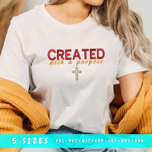 Puede incluir: Camiseta blanca con el texto "CREATED with a purpose" en rojo y dorado, y una cruz dorada. Un suéter color mostaza está drapeado sobre los hombros. La parte inferior de la camiseta muestra "5 SIZES" y formatos de archivos de bordado.