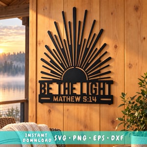 Könnte beinhalten: Ein Wandkunstobjekt aus schwarzem Metall mit einem Sonnenstrahlen-Design über dem Text "BE THE LIGHT" und "MATHEW 5:14". Das Design besteht aus vertikalen Strahlen unterschiedlicher Länge, die von einer halbkreisförmigen Basis ausgehen.