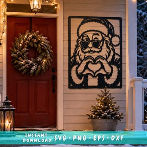 Op de afbeelding: Een zwart metalen wanddecoratie met een uitgesneden ontwerp van de Kerstman die een hartvormige zonnebril draagt en met zijn handen een hartvorm maakt. Het rechthoekige bord is bevestigd aan een lichte muur naast een rode deur met een krans.