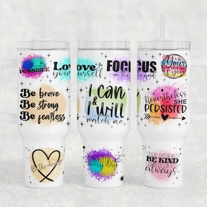 Puede incluir: Tres vasos de acero inoxidable blanco con diseños de acuarela coloridos y citas inspiradoras. Las citas incluyen "Ámate a ti mismo", "Concéntrate en lo bueno", y "Sé valiente, sé fuerte, sé intrépido".