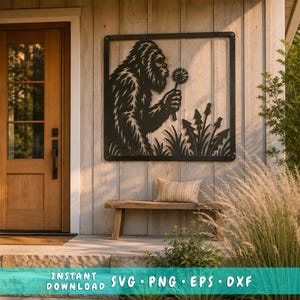 Op de afbeelding: Een zwart metalen wanddecoratie met een silhouet van een Bigfoot die een paardenbloem vasthoudt, omlijst door een vierkante rand. Het ontwerp bevat gestileerd gras en extra paardenbloemen aan de onderkant van de figuur.