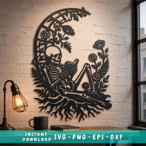 May include: A black laser-cut wall art piece featuring a skeleton sitting and reading a book within a crescent moon frame decorated with flowers, leaves, and roots. The text at the bottom reads: INSTANT DOWNLOAD SVG PNG EPS DXF.