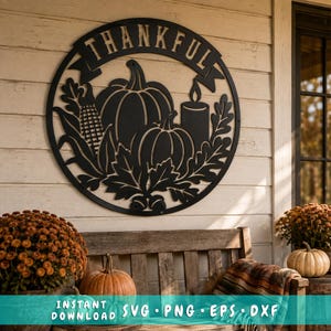May include: A circular black metal wall sign featuring the word THANKFUL in a banner at the top, with a cutout design of two pumpkins, an ear of corn, a candle, and oak leaves. The sign is displayed on a light-colored horizontal wood wall.
