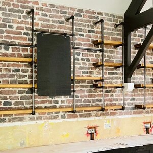 May include: A brick wall with three sets of black metal pipe shelves with wooden shelves. Each set of shelves has a black rectangular sign.