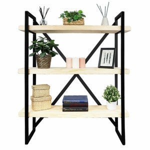 Könnte beinhalten: Ein dreistufiges Holzregal mit schwarzem Metallrahmen. Die Regalbretter sind mit Dekorationsartikeln gefüllt, darunter Pflanzen, Kerzen, Bücher und ein gerahmtes Bild.