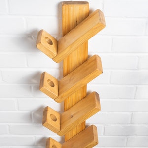 Op de afbeelding: Een houten wandrek voor schoenen met vijf planken. De planken zijn verspringend en schuin geplaatst, wat een uniek ontwerp cre&euml;ert. Het rek is gemaakt van natuurlijk hout en heeft een rustieke uitstraling.