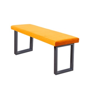 May include: A yellow velvet bench with a dark grey metal frame. The bench has a rectangular seat and square legs.