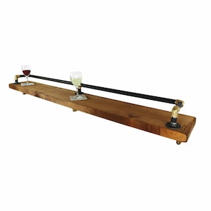 May include: A wooden shelf with a black metal pipe rail. The shelf is mounted to the wall with brass fittings. Two glasses are on the shelf, one with red wine and one with white wine.