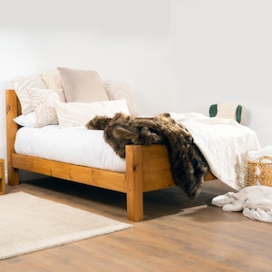 May include: A wooden bed frame with a white duvet and a brown faux fur throw. The bed is styled with several pillows in various shades of beige and white.