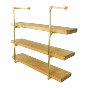 May include: Three-tiered shelf unit with brass pipes and wooden shelves. The shelves are made of natural wood and have a rustic look. The brass pipes are polished and have a shiny finish.