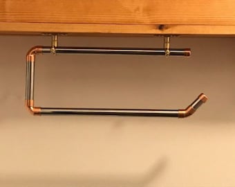 May include: A black metal towel rack with copper accents is mounted to a wooden surface. The rack has a simple design and is perfect for holding towels or other items.