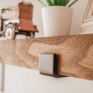 K&ouml;nnte beinhalten: Ein Holzregal mit einer schwarzen Metallhalterung. Das Regal ist aus dunklem Holz mit nat&uuml;rlicher Maserung. Die Halterung ist an der Unterseite des Regals befestigt und hat ein schlichtes, modernes Design.