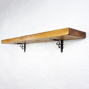Könnte beinhalten: Ein Holzregal mit natürlicher Oberfläche und schwarzen Metallkonsolen. Das Regal ist an einer weißen Backsteinwand montiert.