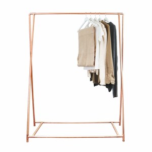 May include: A copper-colored clothing rack with a rectangular base and a top bar for hanging clothes. Several garments in neutral colors hang on white hangers. The rack has a modern, minimalist design.