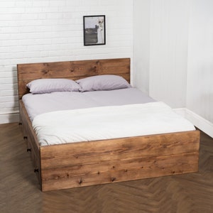 Puede incluir: Un marco de cama de madera con cabecera y piecero. El marco de cama tiene dos cajones en el lateral. La cama est&aacute; hecha de madera natural y tiene un aspecto r&uacute;stico.