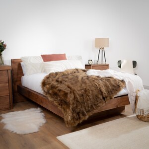 May include: A wooden bed frame with a white duvet and a brown faux fur throw blanket. The bed has a wooden headboard and a white bedside table with a lamp.